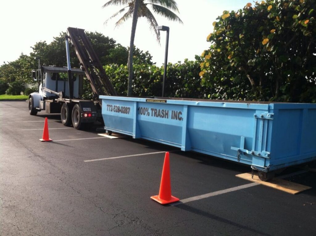 Blue trash dumpster in parking lot with cones