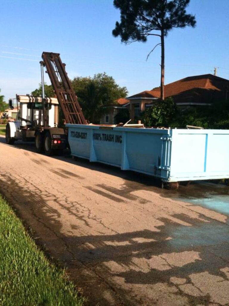 Garbage truck unloading large blue dumpster on street.