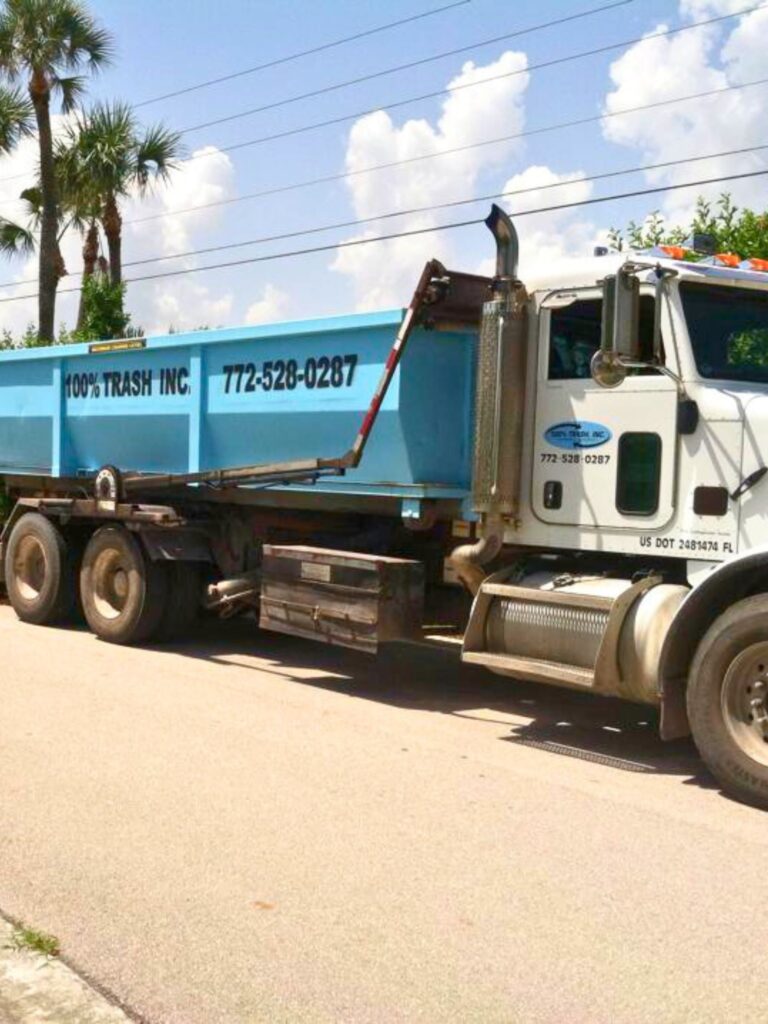 Blue trash truck on sunny day with palm trees.
