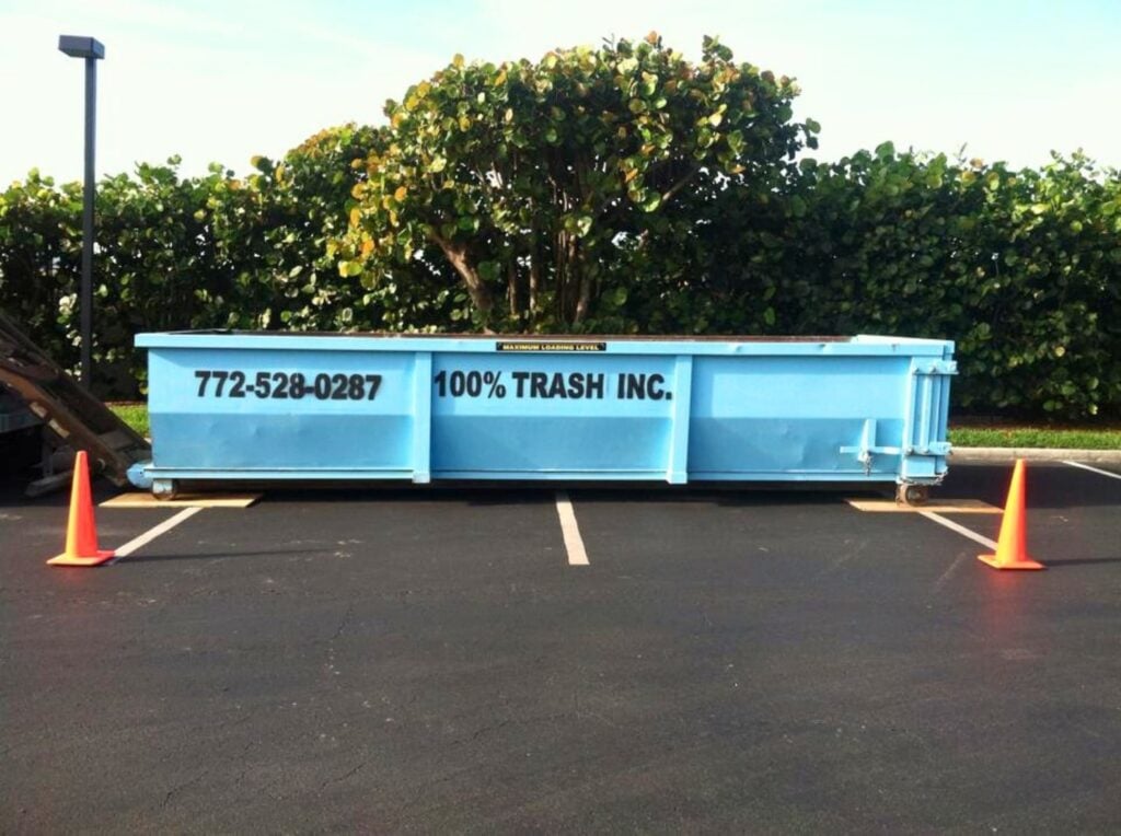 Blue dumpster from 100% Trash Inc. in parking lot.